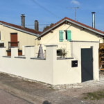 Crépi monocouche Baumit Granicem Light teinte Alger en finition grattée sur murette extérieure avec enduit RPE appliqué sur deux poteaux de portail ronds après préparation du support et pose de baguettes d'angle.